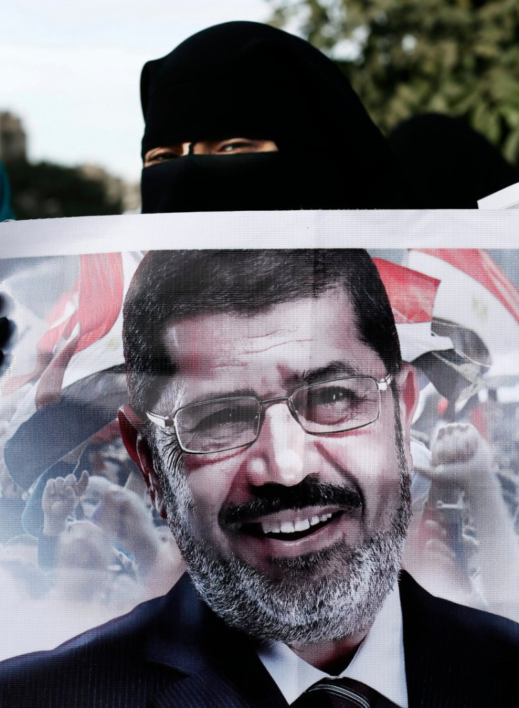 A hooded supporter of Egyptian President Mohammed Morsi peers over the top of a banner with Morsi’s picture during a demonstration Tuesday.