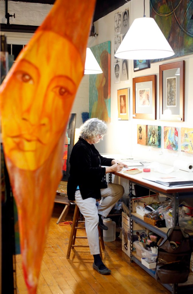 Visual artist Nora Tyron works on a drawing in her studio in the North Dam Mill during the ArtWalk. In the foreground is a piece from a series titled “The Family Tree” created from wood, canvas, stone, and acrylic paint.