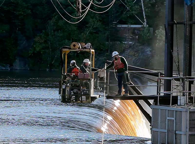 In this file photo, Tyler Grant, right, and Mitch Simpson – both of the Department of Marine Resources – check for salmon atop the Veazie Dam on the Penobscot River in Veazie. Maine will remove the dam as part of the Penobscot River Restoration project.