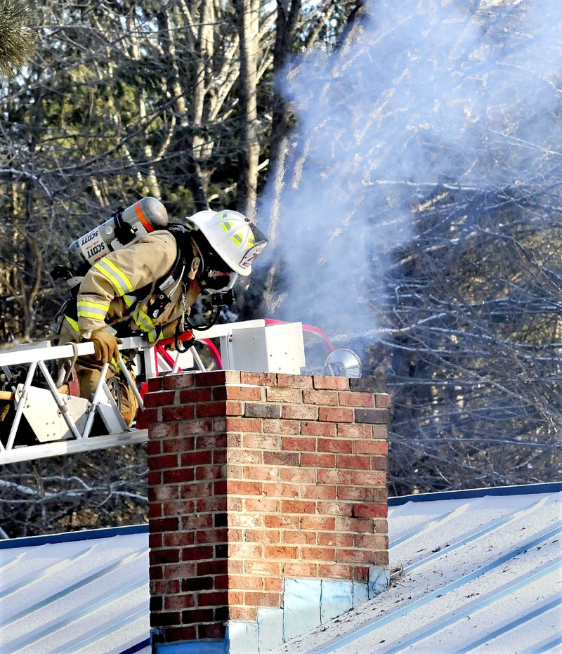 A Winslow firefighter works from a ladder to extinguish a chimney fire at a home on Cushman Road on Tuesday.