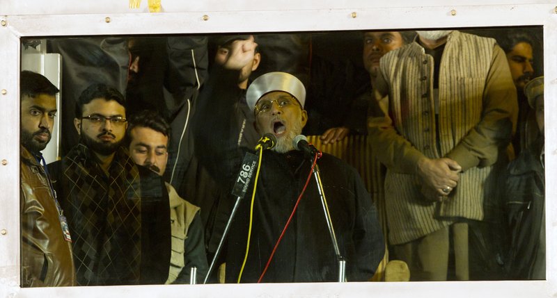 Behind bulletproof glass, Pakistani Sunni Muslim cleric Tahir-ul-Qadri, addresses his supporters about government corruption.
