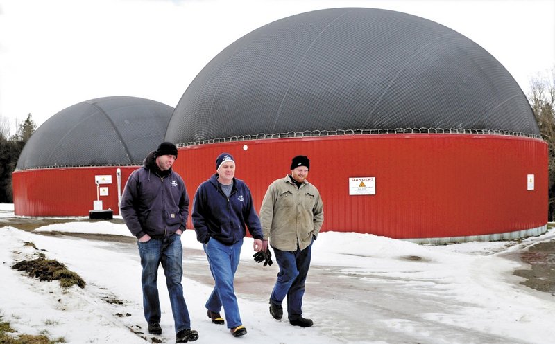 Adam Wintle, left, Travis Fogler and John Wintle walk past the digester buildings where food waste and cow manure are mixed to produce gas that powers a generator for electricity.