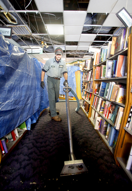 Dustin Souza sucks up the water in the carpet at Longfellow Books in Portland on Sunday. The second-floor sprinkler pipe froze and burst Saturday night during the blizzard, causing extensive water damage to the books and building.