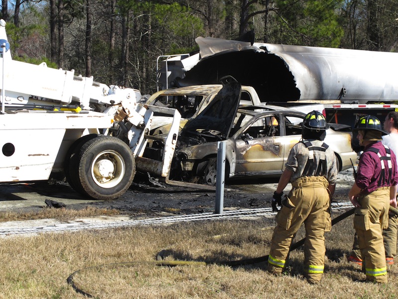 Firefighters stand by as a forklift moves a smashed and burned car at the scene where 27 vehicles collided Wednesday, Feb. 6, 2013, on Interstate 16 near Montrose, Ga. More than two dozen cars, pickup trucks and tractor-trailers collided Wednesday morning in a fiery pileup on a foggy Georgia interstate 16, killing at least three people and sending nine others to a hospital, officials said. (AP Photyo/Russ Bynum)