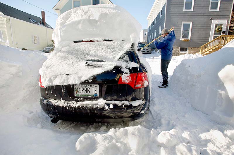 A large snowdrift rests on the top of the car of Joshua Hamel as he cleans off his car in Portland on Sunday, the day after Blizzard Nemo.