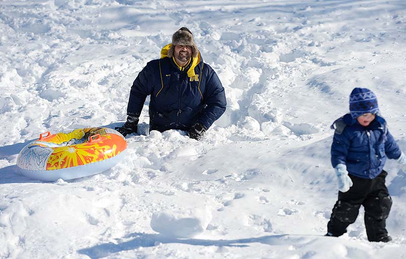Brock Hieger of Saco sinks up to his waist in snow as he walks up a sliding hill at Saco Middle School on Sunday. Heiger was helping his 2-year-old son Gavin, right, when Gavin decided to walk on his own.