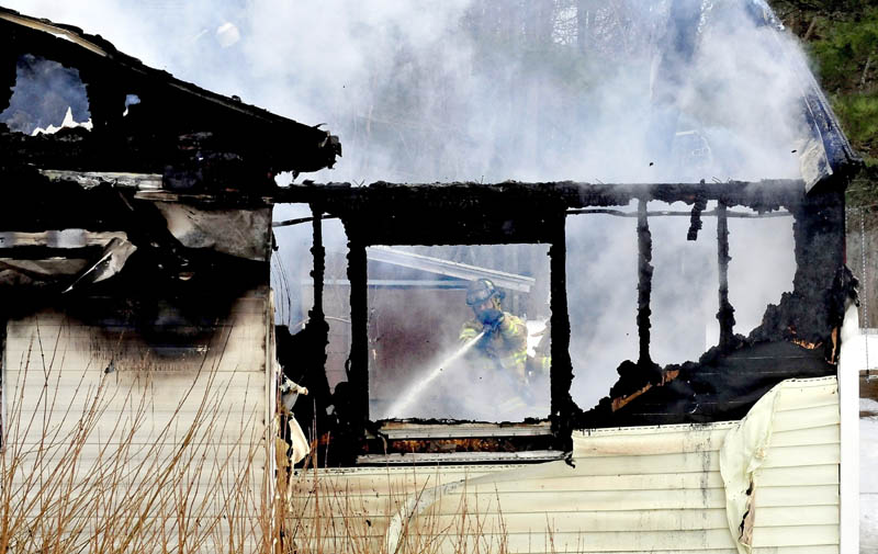 A firefighter can be seen through burned out windows and walls while fighting a fire that destroyed a mobile home Tuesday in Sidney, Maine.