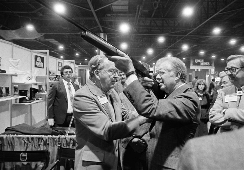 Former President Jimmy Carter sights down the barrel of a shotgun at a gun show in Atlanta in 1984.