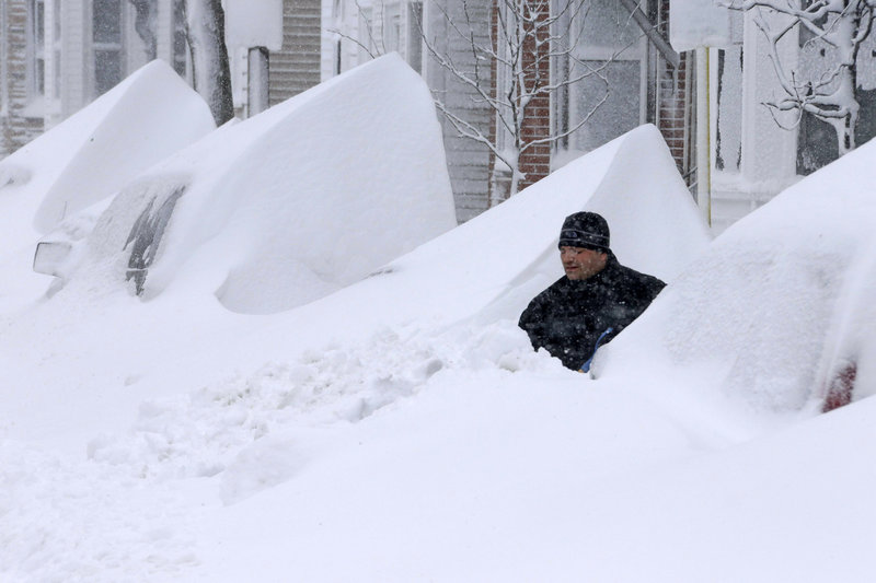 John Silver shovels snow between buried cars in front of his home on Third Street in South Boston on Saturday.