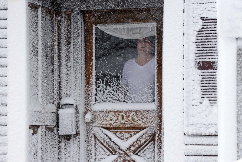 A resident of Third Street in South Boston looks out of his snow-coated front door Saturday.