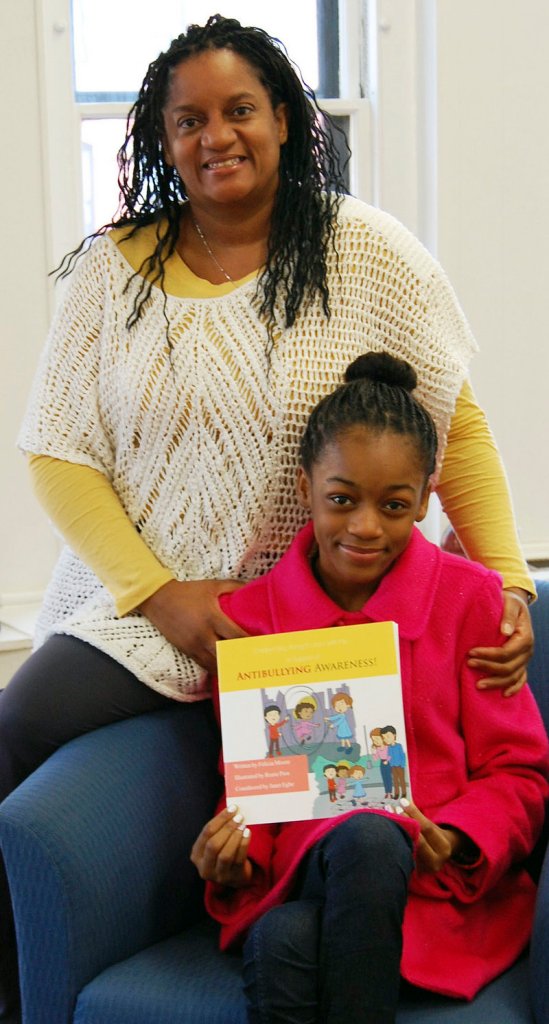 In this Jan. 21, 2013 photo, Felicia Moore, left, poses in Lynn, Mass., with her daughter, Janet Egbe, and a children’s book she wrote about bullying after her daughter was bullied. (AP Photo/Daily Item of Lynn, Chris Stevens)