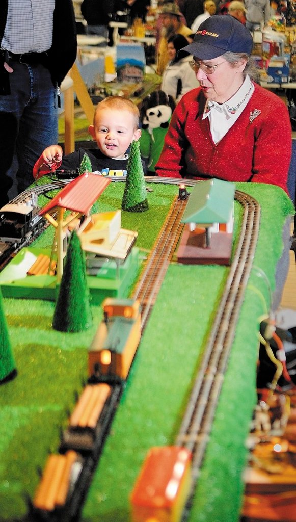 Connor Ruttenberg, 2, of Turner pushes the button to unload logs from a model railroad with some help from Joanne Burns of Friendship at the Maine 3-Railers display Saturday in Augusta.