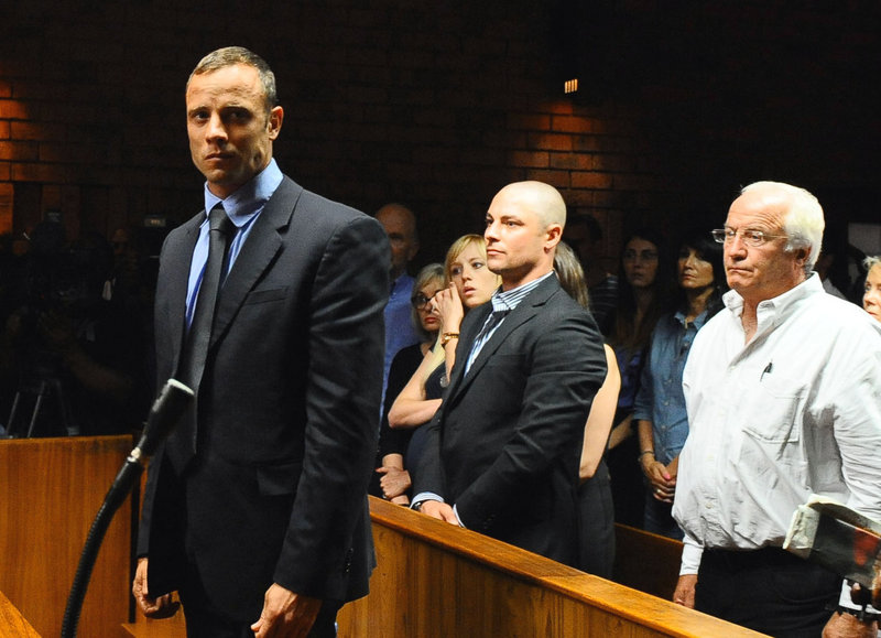 Oscar Pistorius, foreground, stands Tuesday following his bail hearing, in Pretoria, South Africa. He said he shot Reeva Steenkamp after mistaking her for an intruder.