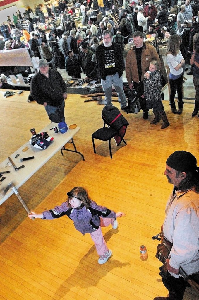 Molly Turnbull, 7, of Knox tosses a tomahawk at a target after getting instructions from Dave “Gomer” Bryant, right, during the Ancient Ones Outdoor Sport and Gun Show on Saturday at the Augusta Armory. Bryant, of Mount Vernon, said that he’s been offering throwing demonstrations for more than 20 years.