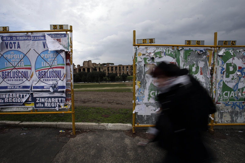 A man walks past election posters in Rome, with the Palatine hill in the background, on Monday. Italy’s crucial elections appear to be heading toward gridlock, initial results show.
