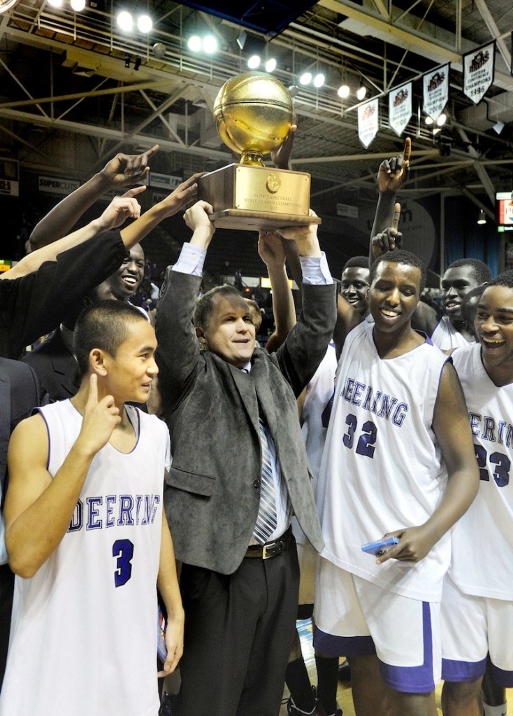 In this March 2012 file photo, Deering head coach Dan LeGage holds the state championship trophy along with his players following their win over Hampden Academy.
