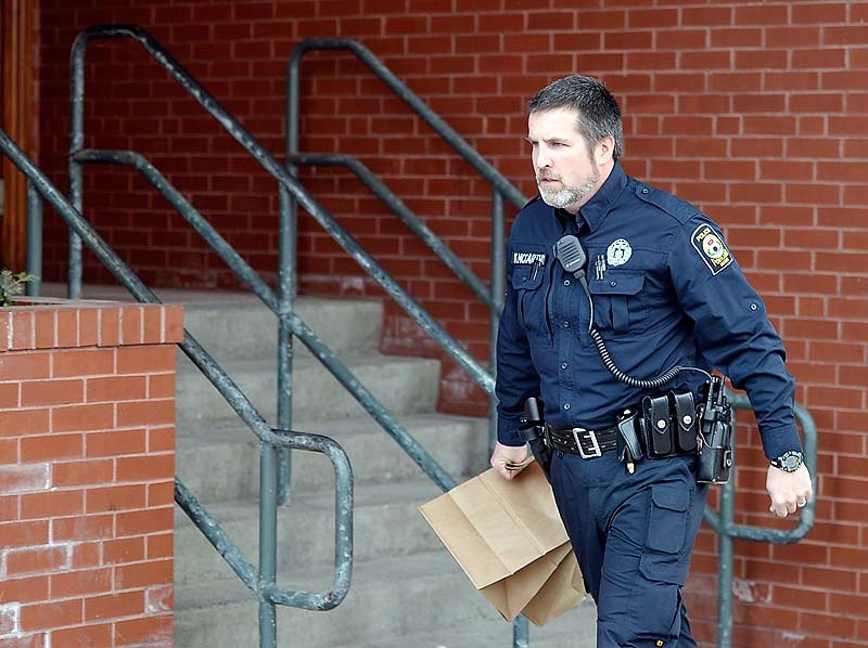 A police officer rushes out of the building with bags of evidence as police surround the Lafayette Square apartment complex in Portland after gunshots were exchanged on the 6th floor on Friday, March 15, 2013.