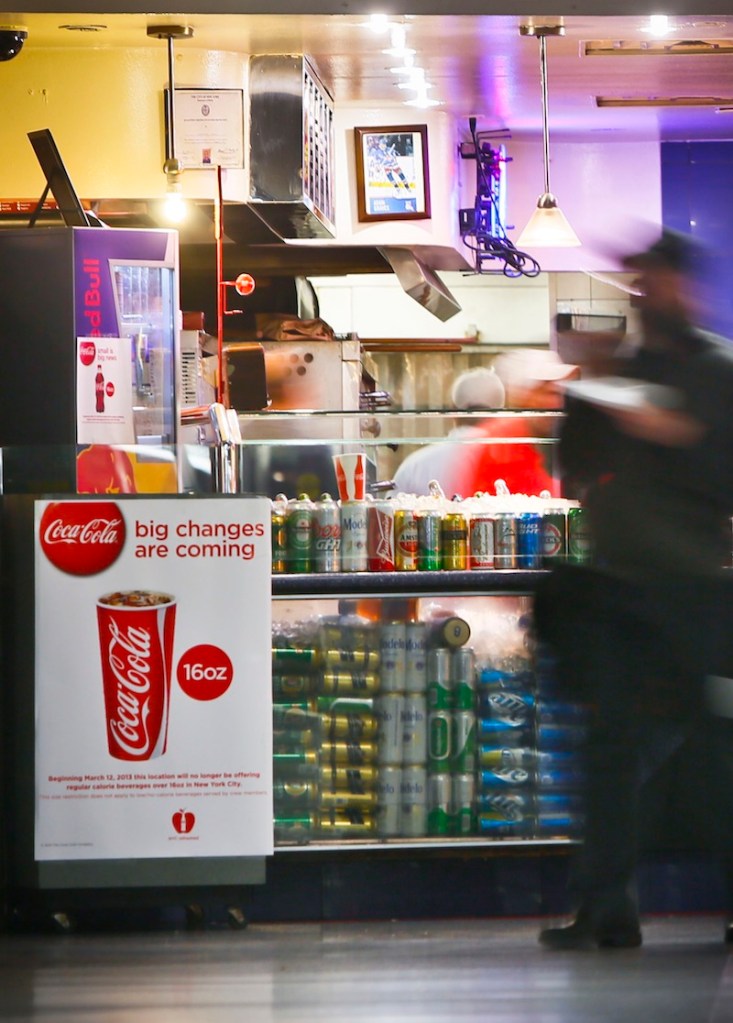 In this March 8, 2013 file photo, a Coca-Cola poster about the city's anticipated beverage ban is displayed at a pizza shop at New York's Penn Station. New York City's groundbreaking limit on the size of sugar-laden drinks has been struck down by a judge shortly before it was set to take effect. The restriction was supposed to start Tuesday, March 12, 2013. The rule prohibits selling non-diet soda and some other sugary beverages in containers bigger than 16 ounces. It applies at places ranging from pizzerias to sports stadiums, though not at supermarkets or convenience stores. (AP Photo/Bebeto Matthews)