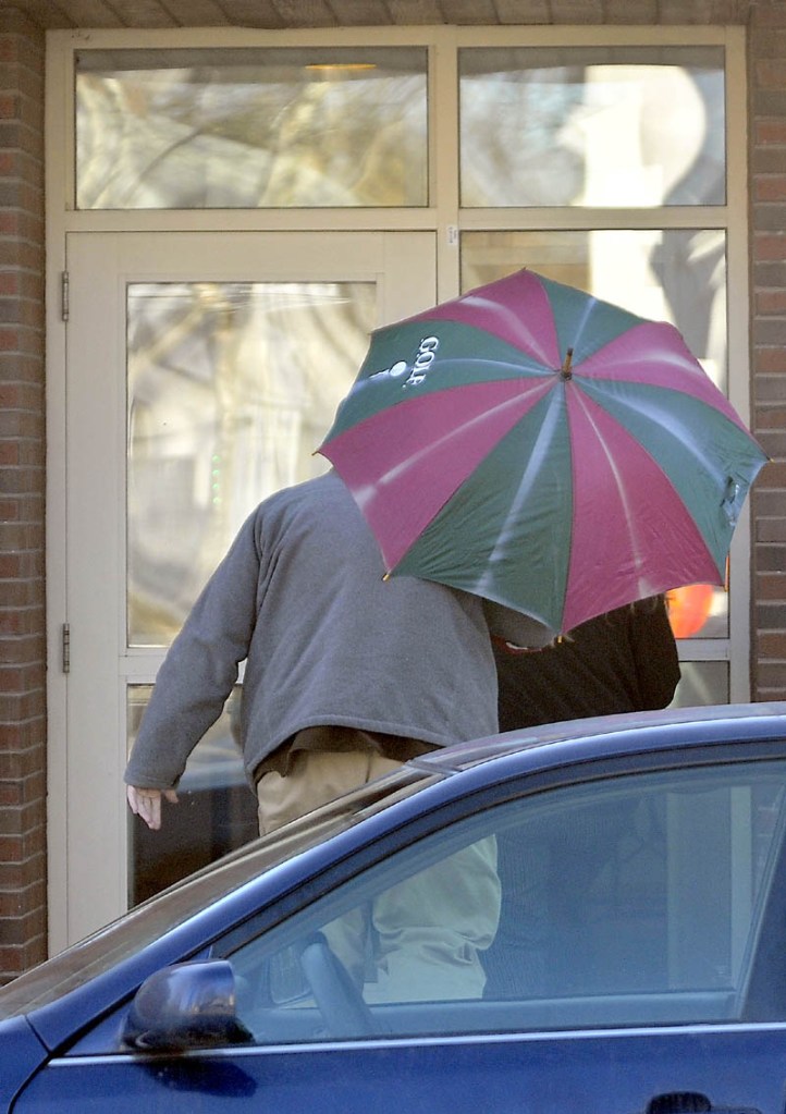 An unidentified man shields Amanda Huard with a striped umbrella as she enters Skowhegan District Court Friday on a sunny morning. Huard is the mother of Kelli Murphy, the 11-year-old charged with manslaughter in the death of an infant last year.