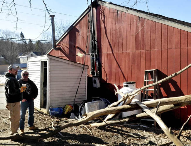 Scott Bouchard, left, speaks with a customer outside his business, Oakland Redemption and Discount Beverage, on Monday. The fallen tree limb, foreground, struck a power line into the building Sunday evening, causing fire that caused extensive damage to the building.