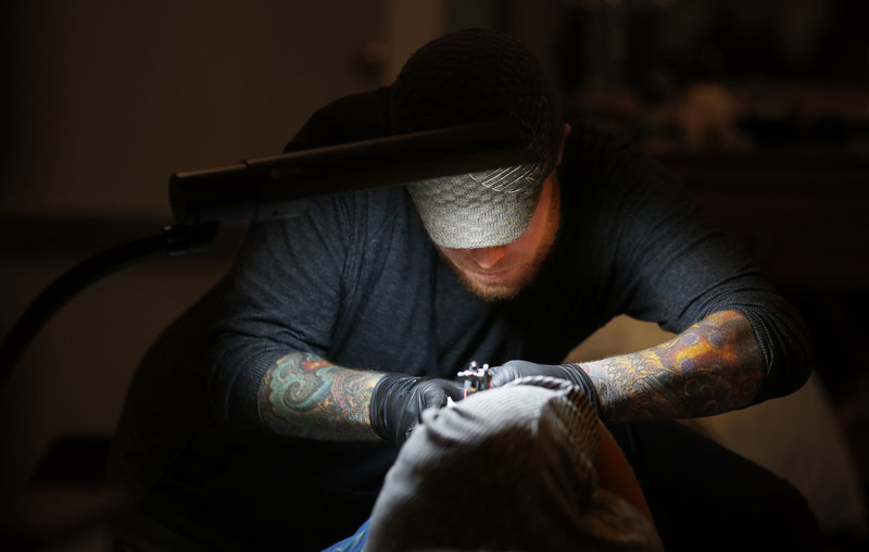 Tattoo artist Mike Rourke of Tsunami Tattoo works on a tattoo for Sharon Boucher of Acton, Mass., Thursday, Feb. 28, 2013, commemorating Boucher's sister, Robyn Hesseltine, who died of ovarian cancer.