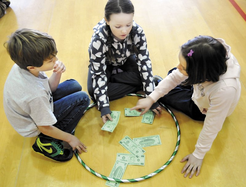 Sullivan Anderson, Miranda Northrup, center, and Abby Peaslee count play money during a game in physical education class at Whitefield Elementary School in Whitefield on Feb. 26.