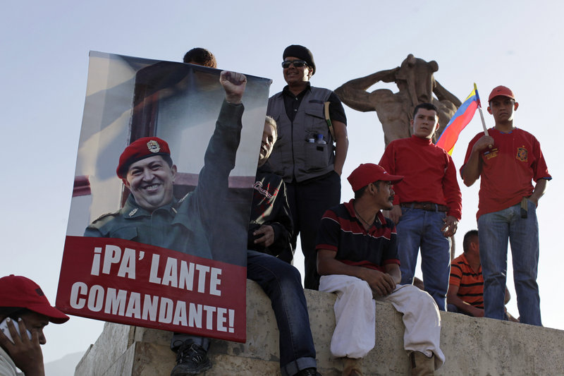 Supporters of Venezuela’s late President Hugo Chavez gather outside a Caracas military academy where leaders from five continents attended a funeral Friday. The poster reads: “Move forward commander!”
