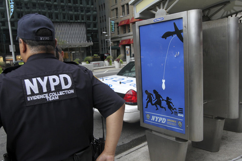 In this September 2012 file photo, New York City police officers wait to remove a fake NYPD "public service" ad at a public phone bank in Lower Manhattan. The ads, installed by Essam "Adam" Attia of Maine, depict the police force as a drone-deploying Big Brother.