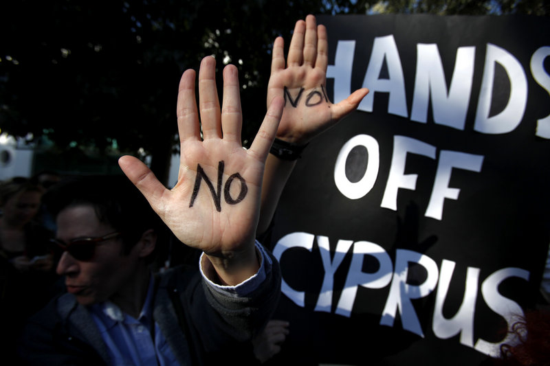 Protesters hold up hands bearing anti-bailout sentiment Monday outside the parliament in Nicosia, Cyprus. A vote on the bailout, which would seize up to 10 percent of savings in Cyprus banks, has been postponed while modification is discussed.