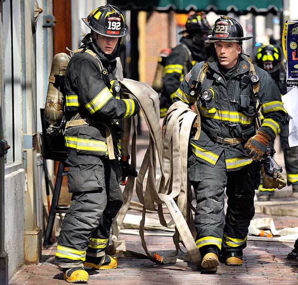 Firefighters drag a hose to the entrance of the Grill Room on Exchange Street Monday, after a fire started in the basement and spread to the walls of the building.