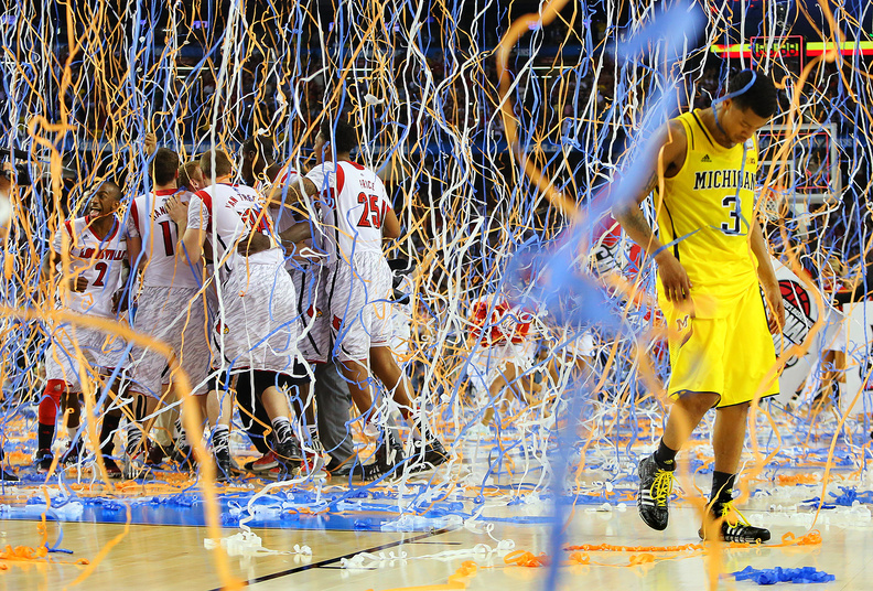 Michigan guard Trey Burke (3) walks off the court as confetti falls on Louisville players, including Russ Smith (2), Luke Hancock (11), Stephan Van Treese (44) and Zach Price (25), after the NCAA Final Four tournament college basketball championship game, Monday in Atlanta. Louisville won 82-76.