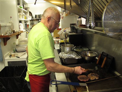 Sherman Sykes cooks hamburgers for a lunchtime crowd at his rebuilt restaurant in Henryville, Ind., recently. The Institute for Supply Management says its index of non-manufacturing activity fell to 54.4 last month from 56 in February.