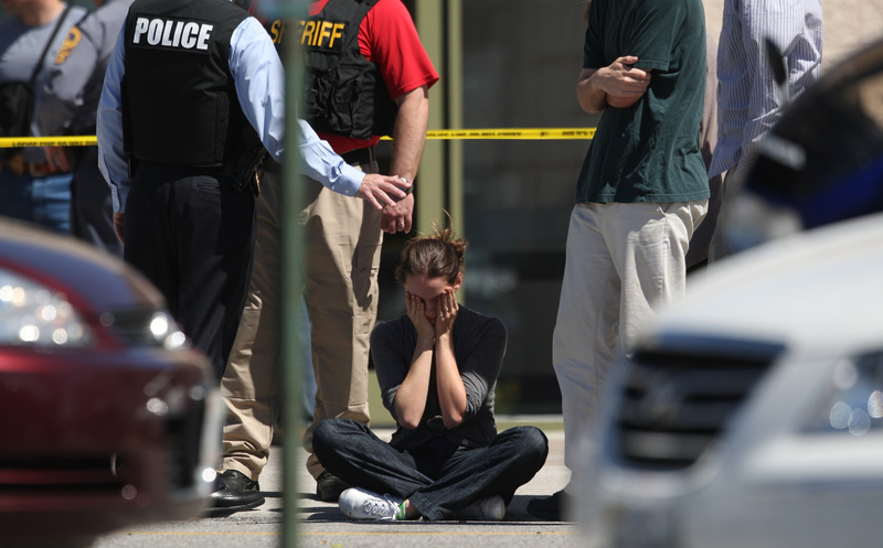 Clara Keller, of Blacksburg, Va., holds her head as she sits on the sidewalk near law enforcement officers outside the New River Valley Mall in Christiansburg, Va., on Friday. VIRGINIA