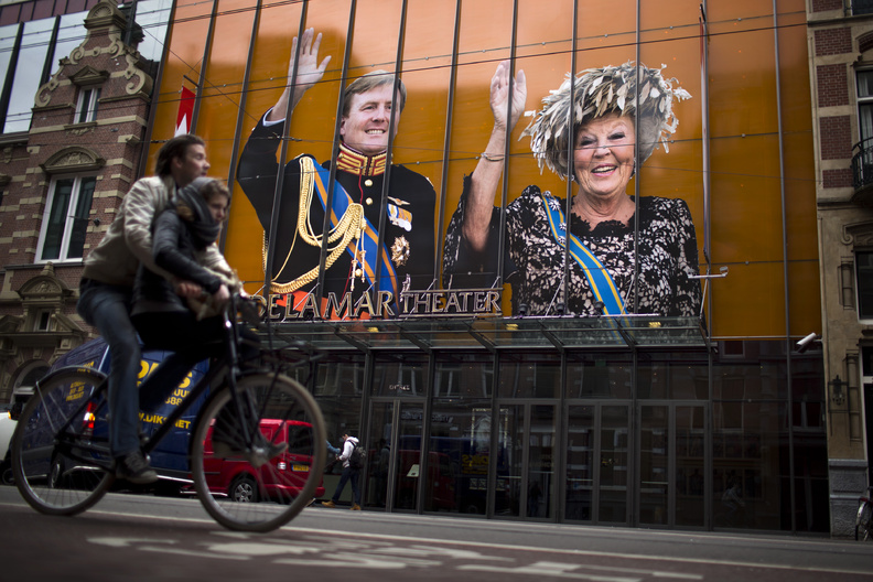 A cyclist passes by an image of Dutch Queen Beatrix and her son Crown Prince Willem-Alexander on the exterior of a theater in downtown Amsterdam, Netherlands, on Monday. Queen Beatrix will relinquish the crown on Tuesday, after 33 years of reign, leaving the monarchy to her son.