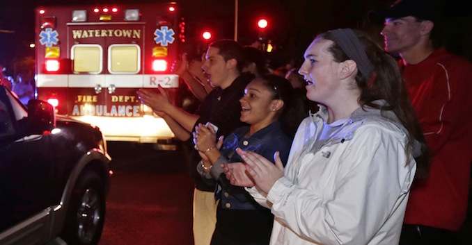A gathering of people applaud as first responders leave the scene after the arrest of a suspect of the Boston Marathon bombings in Watertown, Mass., Friday, April 19, 2013. Two suspects in the Boston Marathon bombing killed an MIT police officer, injured a transit officer in a firefight and threw explosive devices at police during their getaway attempt. (AP Photo/Charles Krupa)