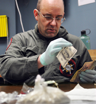 Kennebec County Sheriff's Det. Sgt. Frank Hatch counts money seized during a raid in Farmingdale conducted on Tuesday that resulted in the recovery of more than 100 grams of heroin, in plastic bags. Deputies, agents from the Maine Drug Enforcement and the federal Drug Enforcement Agency arrested four people while seizing the drugs and money from an apartment on Hill Street. The heroin could be packaged sold as approximately 5,000 doses, according to Hatch, with a street value in excess of $50,000.