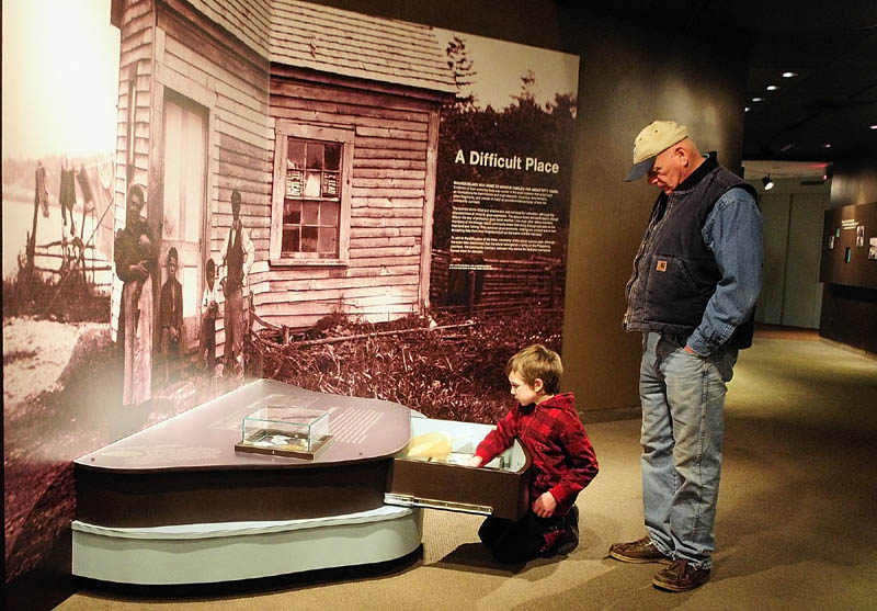 Ciaran Seltsman, 9 of Augusta, left, and his grandfather, Robert Seltsman, of Leeds, look at items in a drawer on Thursday in the "Malaga Island, Fragmented Lives" exhibition at the Maine State Museum in Augusta.