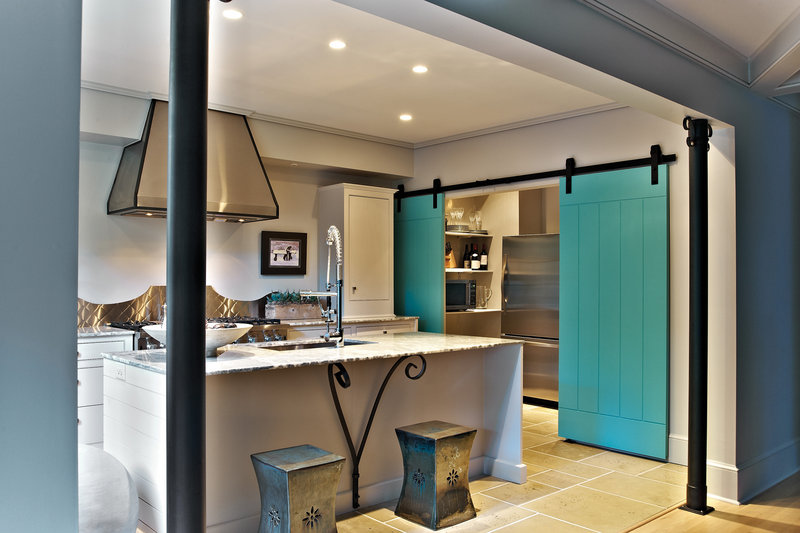 Sliding doors bring a unique look to a room and can be larger and heavier than swinging doors. Blue planks hanging from exposed hardware bring a burst of color and functionality to a kitchen space in this version from Eddie DeRhodes Builder.