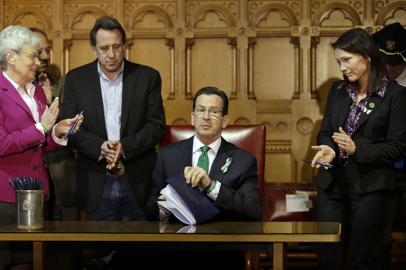 Connecticut Gov. Dannel P. Malloy, center, finishes signing legislation that includes new restrictions on weapons and large-capacity ammunition magazines, at the Capitol in Hartford, Conn., on Thursday. Malloy is applauded by Neil Heslin, father of Sandy Hook shooting victim Jesse Lewis, third from left, Nicole Hockley, right, mother of Sandy Hook School shooting victim Dylan, and Conn. Lt. Gov. Nancy Wyman.