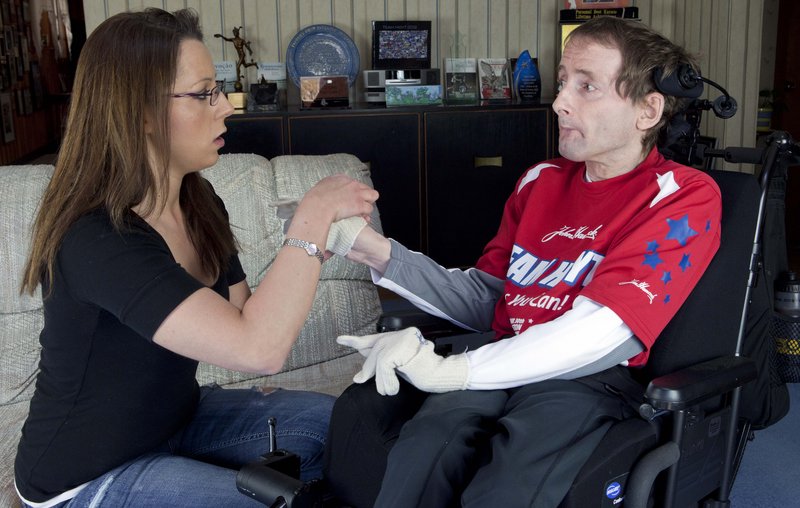 In this April 5, 2013, photo, Rick Hoyt's personal caregiver Lori Templeman, left, helps him put on gloves at his home in Holland, Mass. Hoyt's father Dick has pushed Rick, who is a quadriplegic and has cerebral palsy, in a specially designed wheelchair along the 26.2-mile Boston Marathon route for more than 30 years. They plan to compete again in Monday’s race.