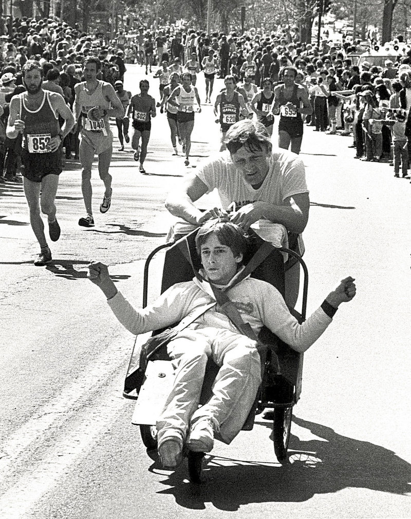 In this circa 1980s photo, Dick Hoyt, rear, pushes his son Rick as they compete in the Boston Marathon, passing along Heartbreak Hill in Newton, Mass.