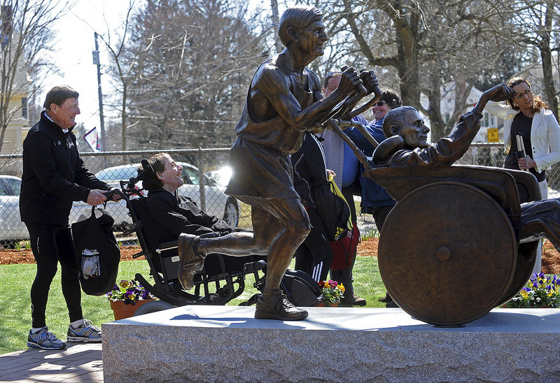 In this April 8, 2013, file photo, Dick Hoyt, left, talks with his son Rick as he wheels him next to a statue dedicated in their honor in front of the Center School in Hopkinton, Mass.