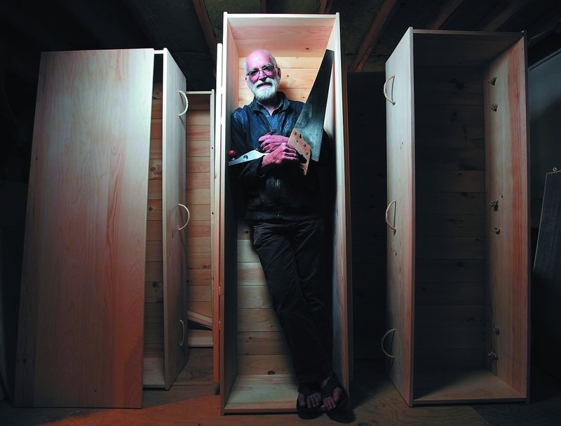 Chuck Lakin stands inside a coffin in the basement workshop of his Waterville home Saturday. “Americans are really good at ignoring the fact that they’re going to die,” he said.