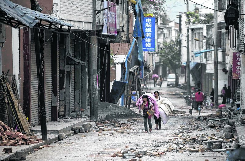 People carrying their belongings walk in quake-damaged Gucheng Village, Longmen Township, Lushan county, in southwest China’s Sichuan Province on Saturday.