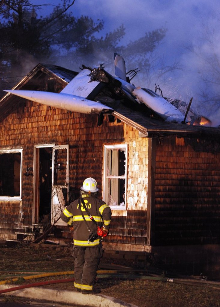 In this 2011 file photo, firefighters extinguish a blaze on Granite Street in Biddeford after a plane crashed into a home. The children of a highly decorated, retired Air Force pilot who died when his civilian plane crashed in Biddeford two years ago, and the couple whose home was destroyed by the crash, are jointly suing the companies that maintained and inspected the plane.