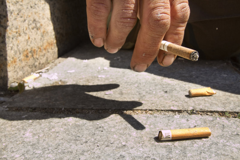 A Monument Square smoker flips his ashes on the ground near some illegally disposed cigarette butts. A Monument Square business owner is trying to institute a program that pays 5 cents per cigarette butt to keep the square clean.