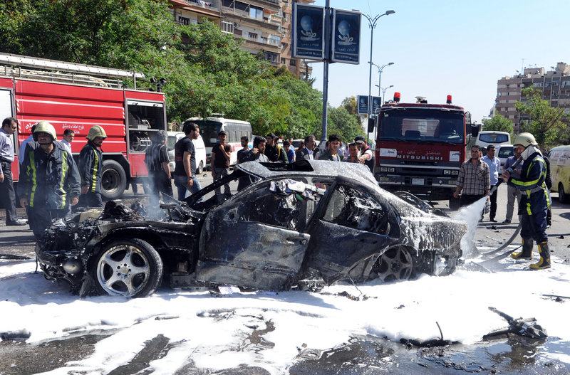 A photo released by the Syrian official news agency SANA shows firefighters extinguishing burning vehicles after a car bomb exploded in the posh capital neighborhood of Mazzeh.