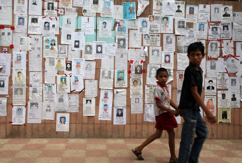 Two boys walk past a wall pasted with fliers showing some of the missing in the Savar, Bangladesh, building collapse. Rescuers on Monday gave up hope of finding more survivors.