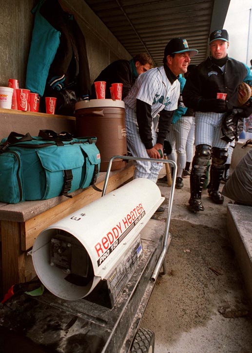 FILE PHOTO BY JOHN EWING --APRIL 6,1995-Portland Sea Dogs manager Carlos Tosca takes advantage of a dugout heater during last season's home opener. Next to him is returning catcher Mike Redmond.