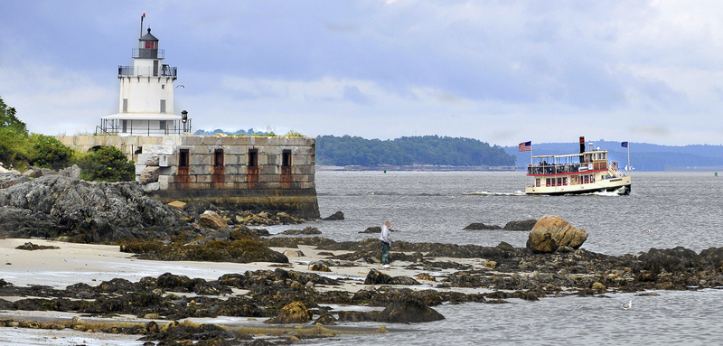 A tourist boat passes Spring Point Ledge Lighthouse as a solitary visitor enjoys Willard Beach near Fort Preble in South Portland.